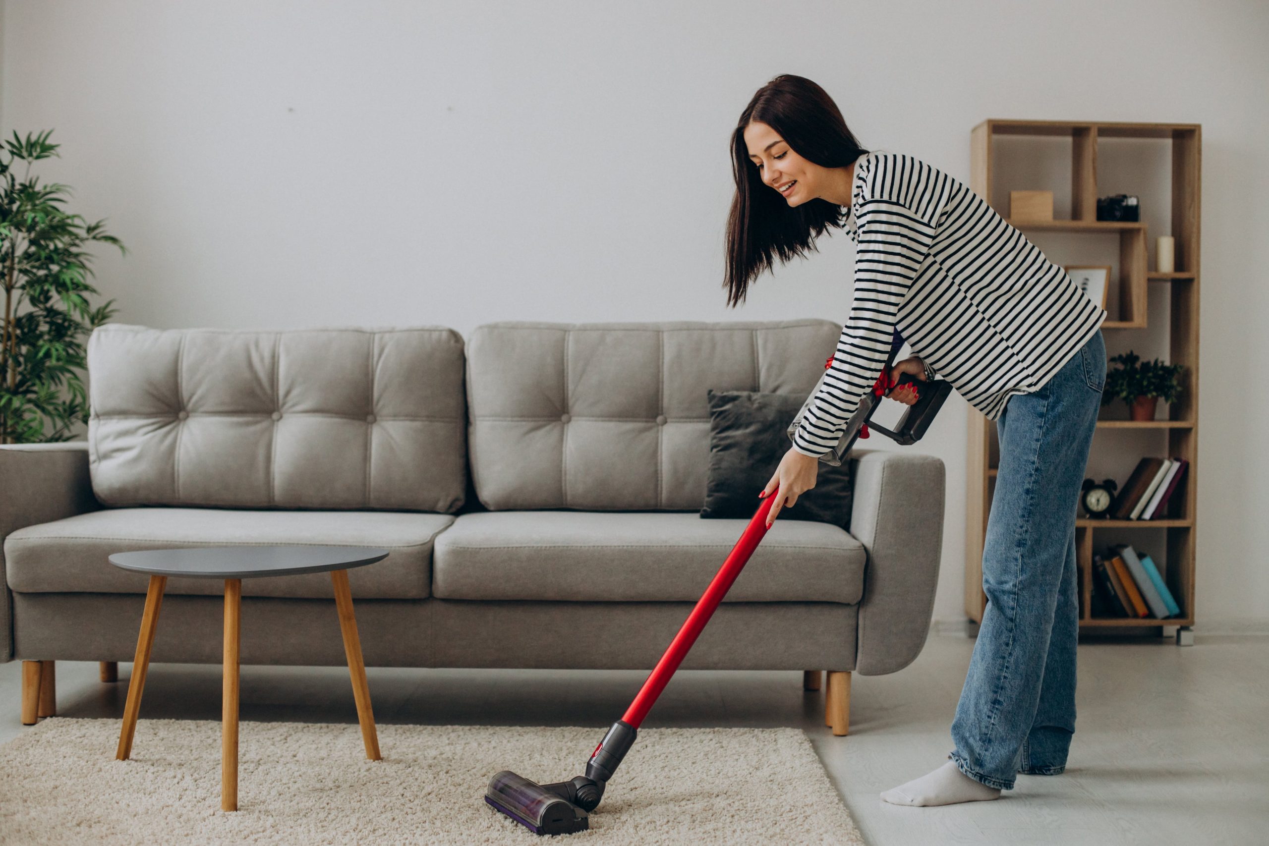 Woman cleaning carpet with cordless vacuum cleaner in modern living roomWoman cleaning carpet with cordless vacuum cleaner in modern living room