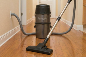 Using a central vacuum floor brush to gently clean dust and debris from polished hardwood flooring in a residential hallway.